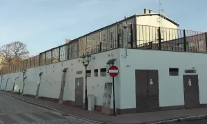 Budynek z kratami na dachu, przypominający poprawczak. Na ścianie znaki zakazu, drzwi i lampy uliczne.