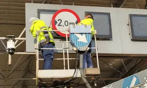 Pracownicy na podnośniku montują znak ograniczenia wysokości 2,0m przy bramkach viatoll.