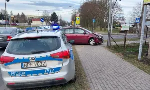 Samochód policyjny z włączonymi sygnałami świetlnymi przy czerwonym samochodzie po kolizji drogowej.