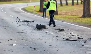 Na drodze po kolizji leżą szczątki, opona i inne elementy. Policjanci w kamizelkach odblaskowych badają miejsce zdarzenia, być może szukając śladów ucieczki z miejsca kolizji.