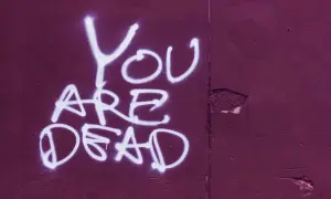 Napis "You ARE DEAD" białą farbą na fioletowej ścianie. Groźba karalna, która budzi niepokój.