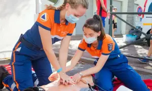 Dwie ratowniczki w maskach ćwiczą resuscytację krążeniowo-oddechową (KPP) na fantomie.