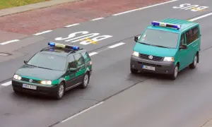 Dwa pojazdy uprzywilejowane Straży Granicznej na drodze. Jeden to ciemnozielony Volkswagen Passat kombi, drugi to turkusowy Volkswagen Transporter.