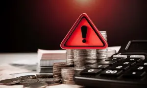 Czerwony znak ostrzegawczy na stosach monet i kalkulatorze.