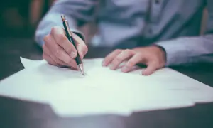 Dłoń pisze piórem na dokumencie. Może to być akt poświadczenia dziedziczenia, ważny dokument prawny.