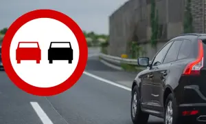 Znak zakaz wyprzedzania na drodze. Czerwony okrąg z dwoma samochodami symbolizuje zakaz wyprzedzania.