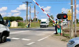 Pracownik obsługuje przejazd kolejowy z zaporami. Czerwone światło sygnalizatora i opuszczone bariery zatrzymują ruch pojazdów.