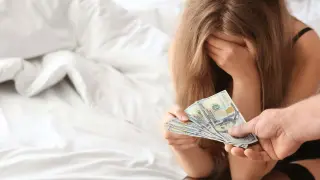 Kobieta z ręką na twarzy otrzymuje pieniądze, co sugeruje stręczycielstwo.
