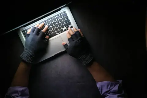 Ręce w rękawiczkach bez palców piszą na laptopie, szukając informacji, co może prowadzić do doxxingu.