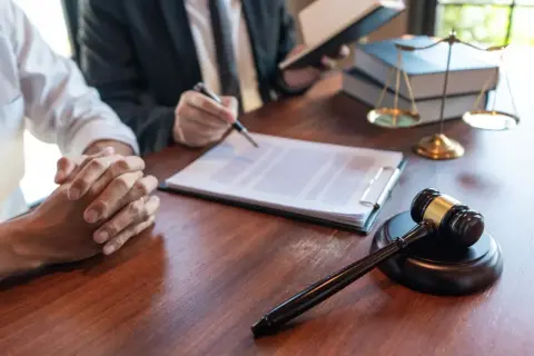 Prawnik omawia testament, który jest częścią spadku po rodzicach. Na stole młotek sędziowski i waga sprawiedliwości.