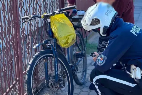 Policjant sprawdza rower na drodze dla rowerów. Żółta torba wisi na kierownicy.