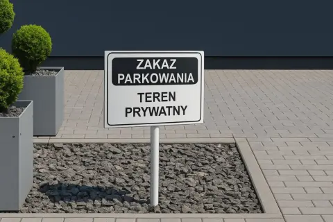 Znak "Zakaz parkowania, teren prywatny" na drodze wewnętrznej. Obok ozdobne krzewy w donicach.