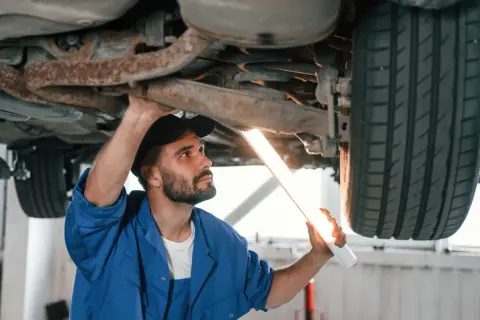 Mechanik z latarką bada podwozie auta. Upewnia się, że nie ma **braku przeglądu powyżej 30 dni**, by zapewnić bezpieczeństwo.