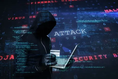 Sylwetka hakera w kapturze, trzymająca laptopa i kartę kredytową. W tle widać kod i napisy "ATTACK", "VIRUS", "MALWARE", "SECURITY", sugerujące atak hakerski.