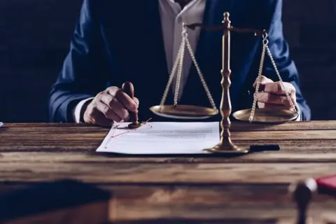Mężczyzna w garniturze stempluje dokument obok wagi sprawiedliwości.