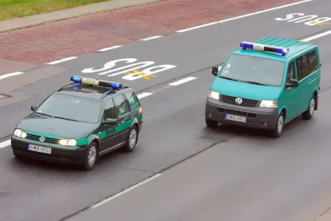 Dwa pojazdy uprzywilejowane Straży Granicznej na drodze. Jeden to ciemnozielony Volkswagen Passat kombi, drugi to turkusowy Volkswagen Transporter.