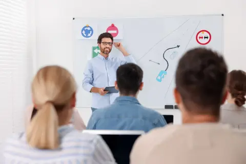 Nauczyciel prowadzi kurs reedukacyjny, tłumacząc zasady ruchu drogowego na tablicy. Uczestnicy słuchają uważnie.
