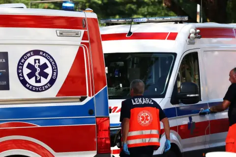 Dwie karetki pogotowia, ratownicy medyczni w kamizelkach odblaskowych.