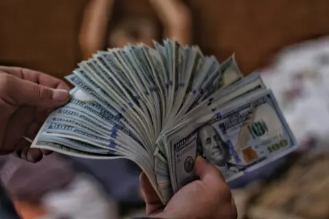 Dłonie trzymają wachlarz banknotów 100-dolarowych, sugerując pranie pieniędzy.