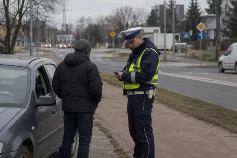 Policjant kontroluje kierowcę stojącego przy samochodzie. Dowiedz się, co grozi za jazdę bez prawa jazdy po jego zatrzymaniu.