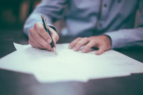 Dłoń pisze piórem na dokumencie. Może to być akt poświadczenia dziedziczenia, ważny dokument prawny.