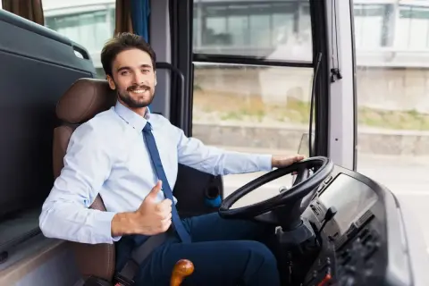 Uśmiechnięty kierowca autobusu, w białej koszuli i granatowym krawacie, pokazuje kciuk w górę. Jego czas pracy przebiega spokojnie.