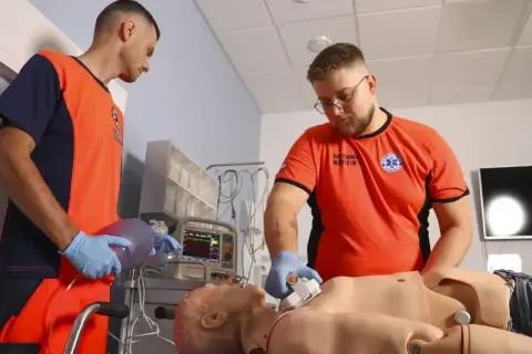 Uczestnicy kursu ratownika medycznego ćwiczą resuscytację na fantomie. Jeden z nich przygotowuje maskę oddechową, drugi uciska klatkę piersiową.