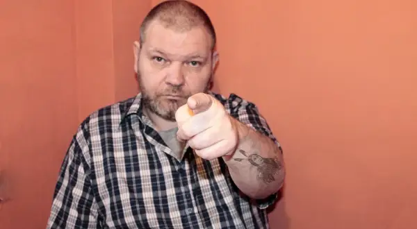 Mężczyzna w kratę wskazuje palcem, na ramieniu tatuaż z Indianinem. "234 kk" - czy to jego numer?