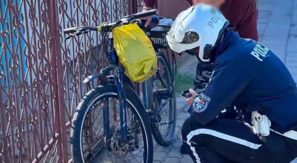 Policjant sprawdza rower na drodze dla rowerów. Żółta torba wisi na kierownicy.