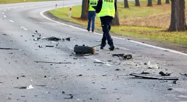 Na drodze po kolizji leżą szczątki, opona i inne elementy. Policjanci w kamizelkach odblaskowych badają miejsce zdarzenia, być może szukając śladów ucieczki z miejsca kolizji.