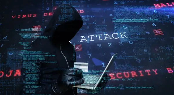 Sylwetka hakera w kapturze, trzymająca laptopa i kartę kredytową. W tle widać kod i napisy "ATTACK", "VIRUS", "MALWARE", "SECURITY", sugerujące atak hakerski.
