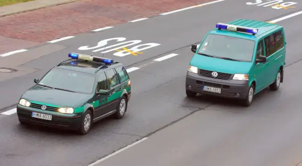 Dwa pojazdy uprzywilejowane Straży Granicznej na drodze. Jeden to ciemnozielony Volkswagen Passat kombi, drugi to turkusowy Volkswagen Transporter.