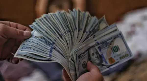 Dłonie trzymają wachlarz banknotów 100-dolarowych, sugerując pranie pieniędzy.
