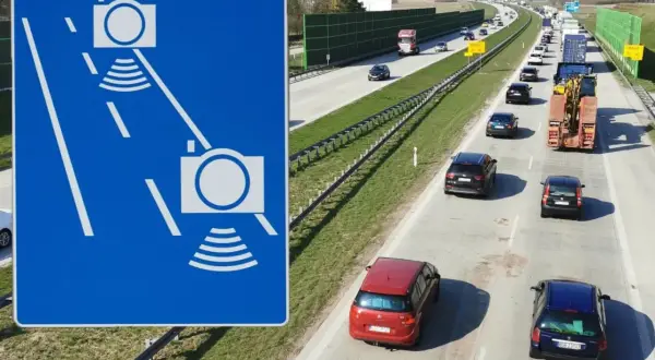 Niebieski znak z białymi ikonami kamer i falami, obok autostrady z ruchem samochodowym.
