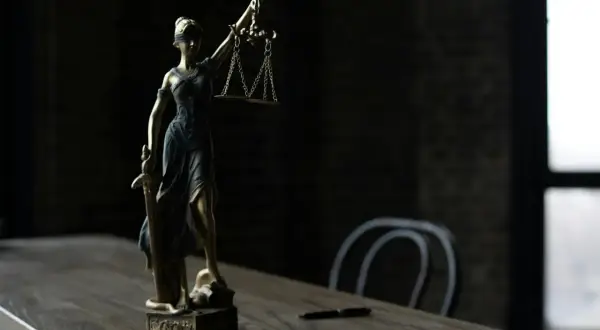 Figurka Temidy z wagą i mieczem na drewnianym stole.