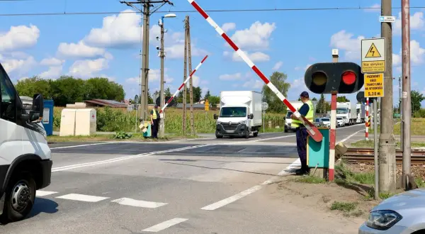 Pracownik obsługuje przejazd kolejowy z zaporami. Czerwone światło sygnalizatora i opuszczone bariery zatrzymują ruch pojazdów.