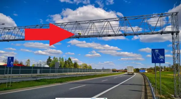 Na A4, pod niebieskim niebem z chmurami, widać bramownicę z urządzeniem do odcinkowego pomiaru prędkości. Czerwona strzałka wskazuje na system monitorowania.