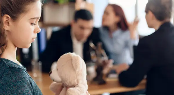 Smutna dziewczynka z misiem w ramionach, w tle kłócący się rodzice i kurator sądowy.