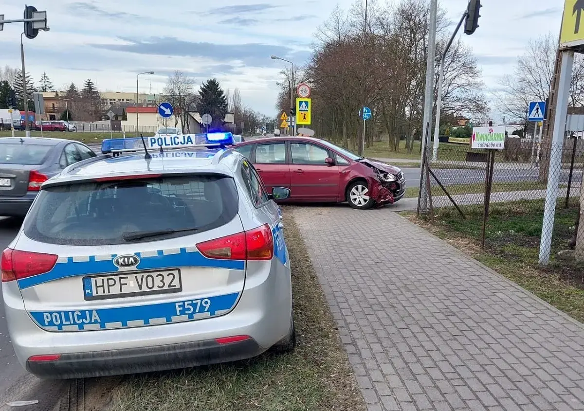 Samochód policyjny z włączonymi sygnałami świetlnymi przy czerwonym samochodzie po kolizji drogowej.