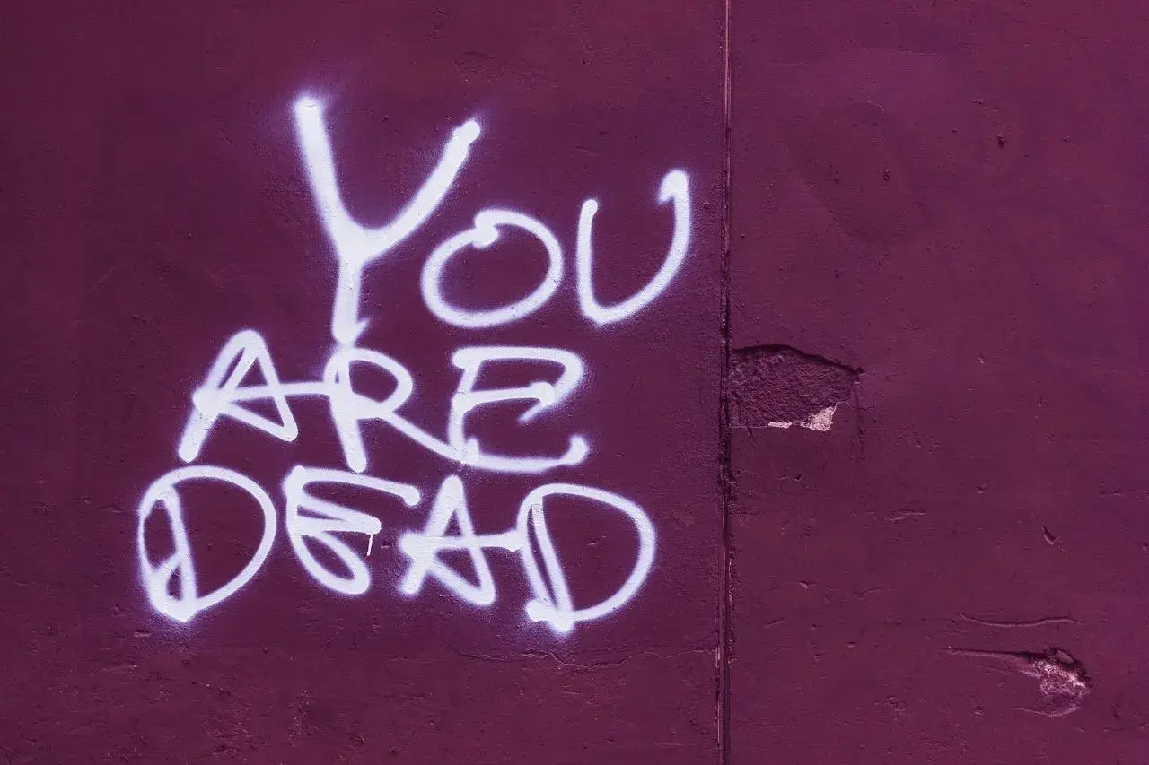 Napis "You ARE DEAD" białą farbą na fioletowej ścianie. Groźba karalna, która budzi niepokój.