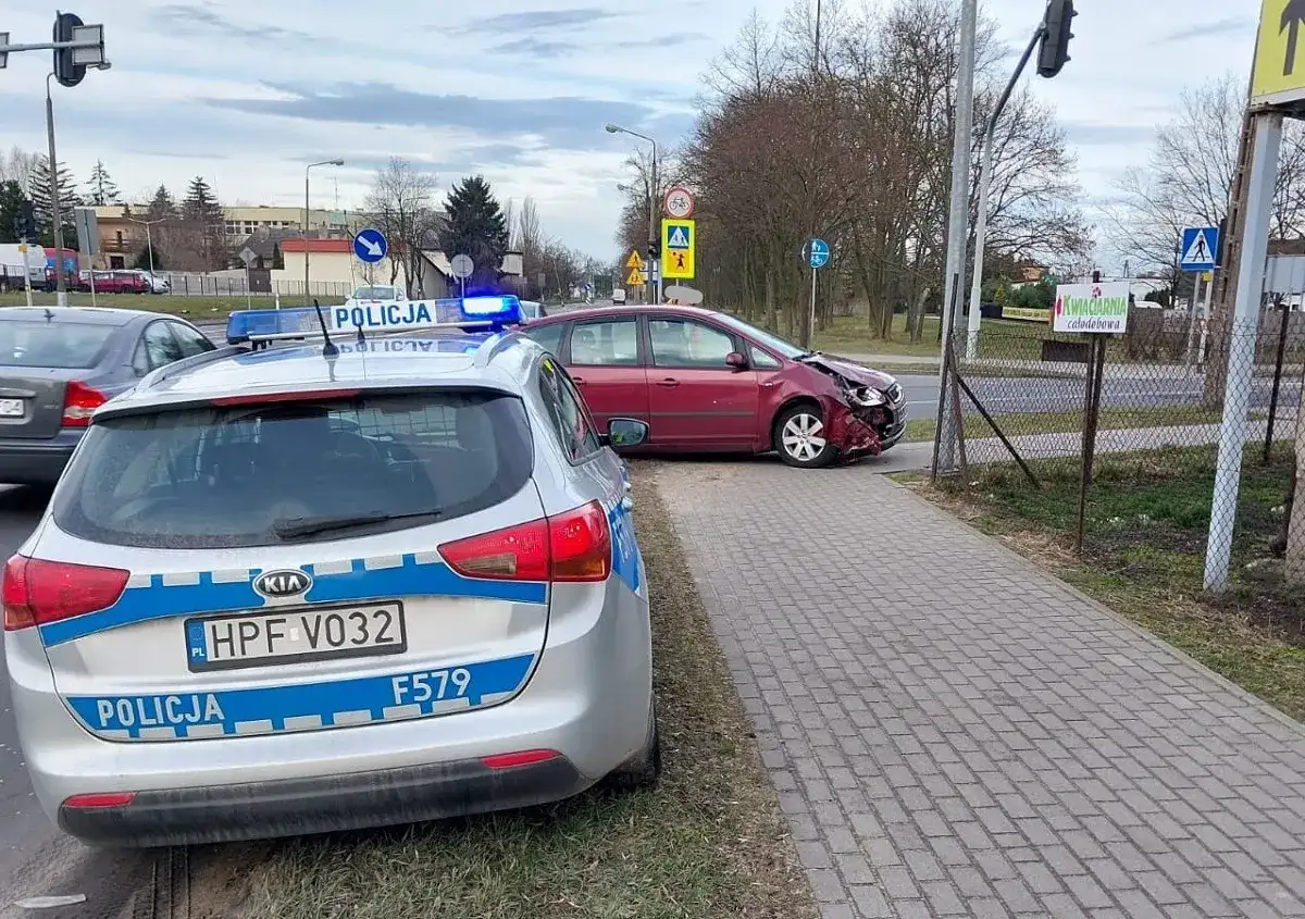 Samochód policyjny z włączonymi sygnałami świetlnymi przy czerwonym samochodzie po kolizji drogowej.