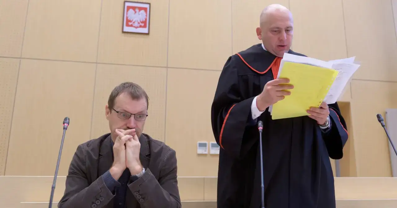 Sąd przesłuchuje świadka koronnego. Mężczyzna w okularach z dłońmi złożonymi na ustach słucha sędziego w todze, który czyta dokumenty.