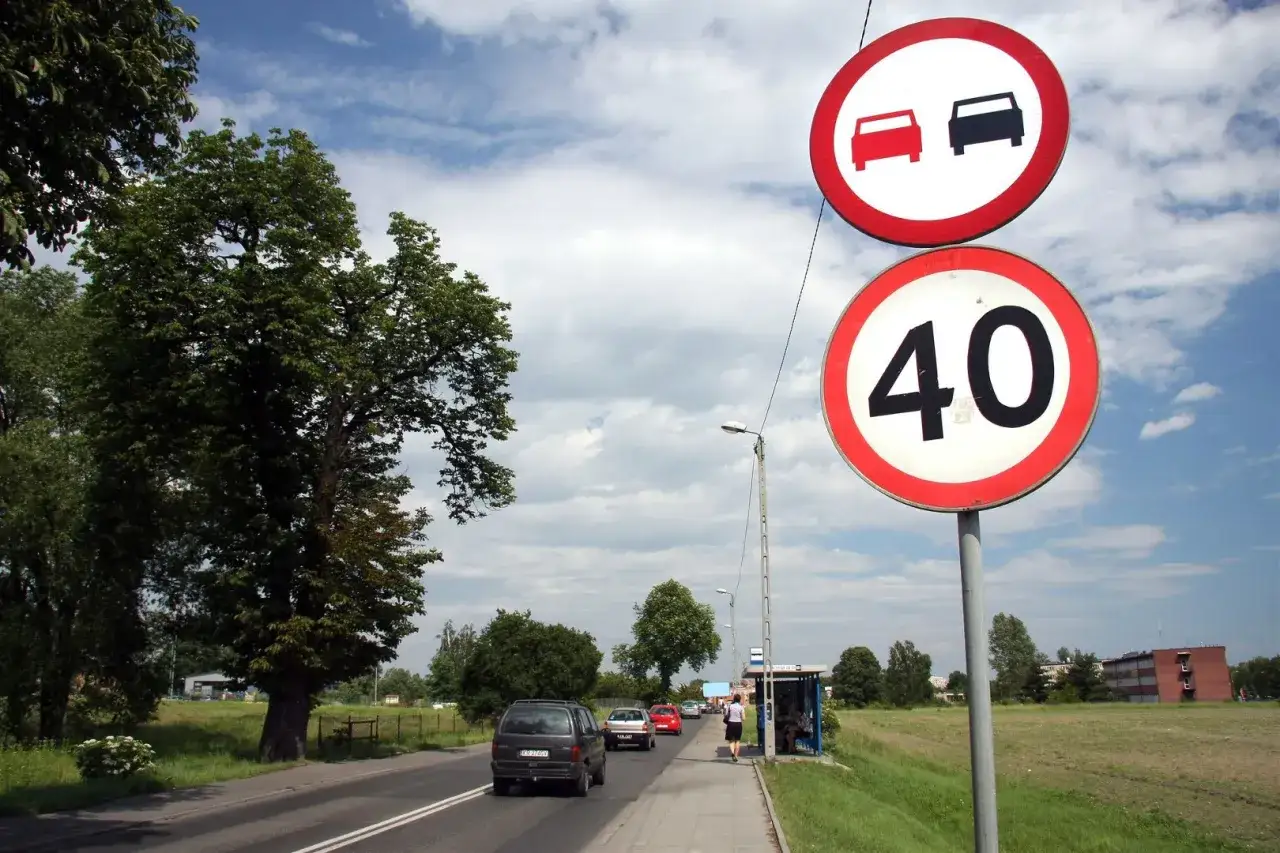 Znak zakaz wyprzedzania i ograniczenie prędkości do 40 km/h. Samochody jadą drogą obok zieleni.
