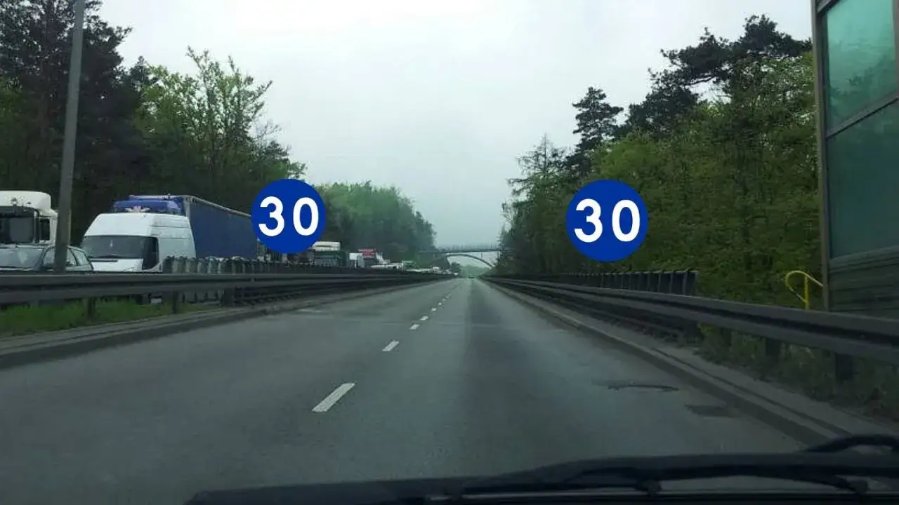 Autostrada z ruchem drogowym i znakami informującymi o minimalnej prędkości na autostradzie 30 km/h.