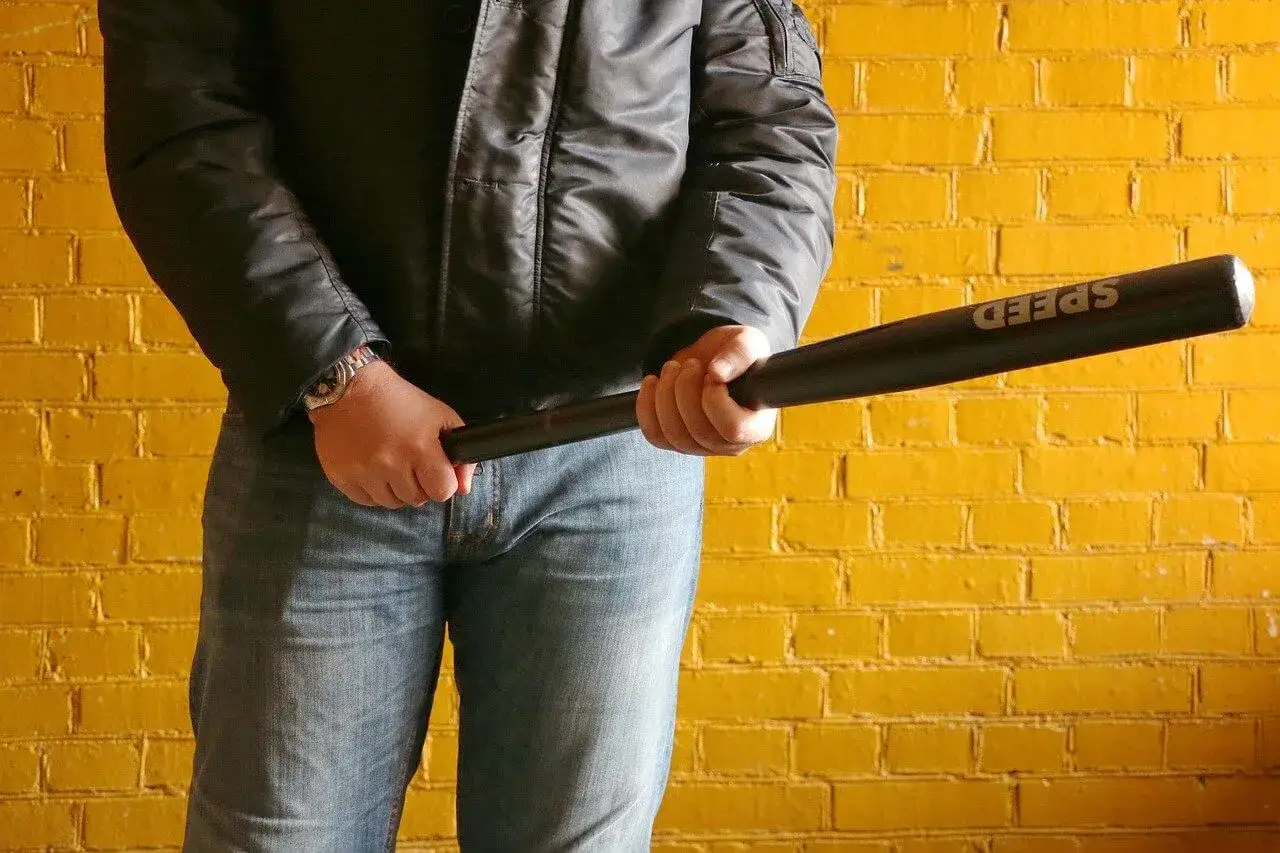 Mężczyzna w kurtce i jeansach trzyma kij baseballowy z napisem
