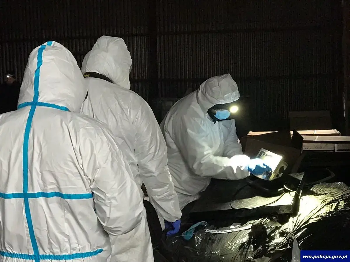 Osoby w kombinezonach ochronnych badają teren z latarkami. Wśród nich znajduje się sprzęt, który może być powiązany z 3cmc.