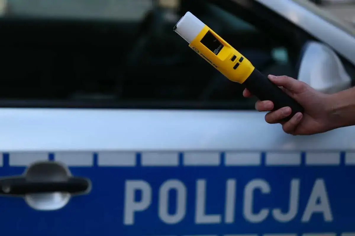 Policjant trzyma alkomat przy radiowozie. Dbałość o limit alkoholu w Polsce to bezpieczeństwo na drogach.