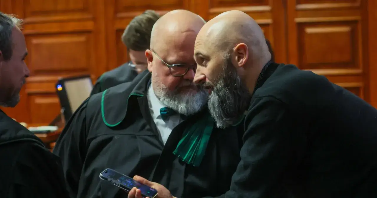 Dwóch mężczyzn w togach prawniczych dyskutuje, jeden pokazuje drugiemu coś na telefonie. Może to być kluczowy świadek koronny.