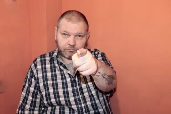 Mężczyzna w kratę wskazuje palcem, na ramieniu tatuaż z Indianinem. "234 kk" - czy to jego numer?