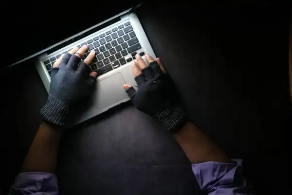 Ręce w rękawiczkach bez palców piszą na laptopie, szukając informacji, co może prowadzić do doxxingu.